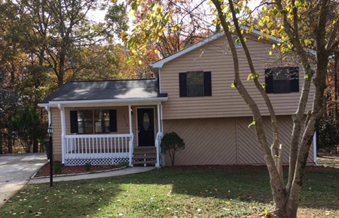 a tan house with a white porch and a tree